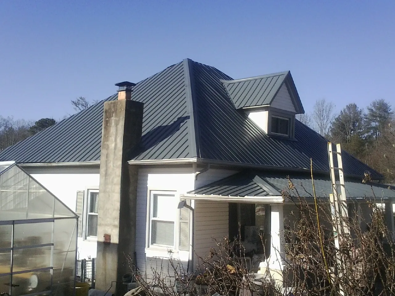 Dark blue standing seam metal roof on a white farmhouse with dormer — Slate & Tile Roof Repair by Roofing Brothers in Mountain Dale