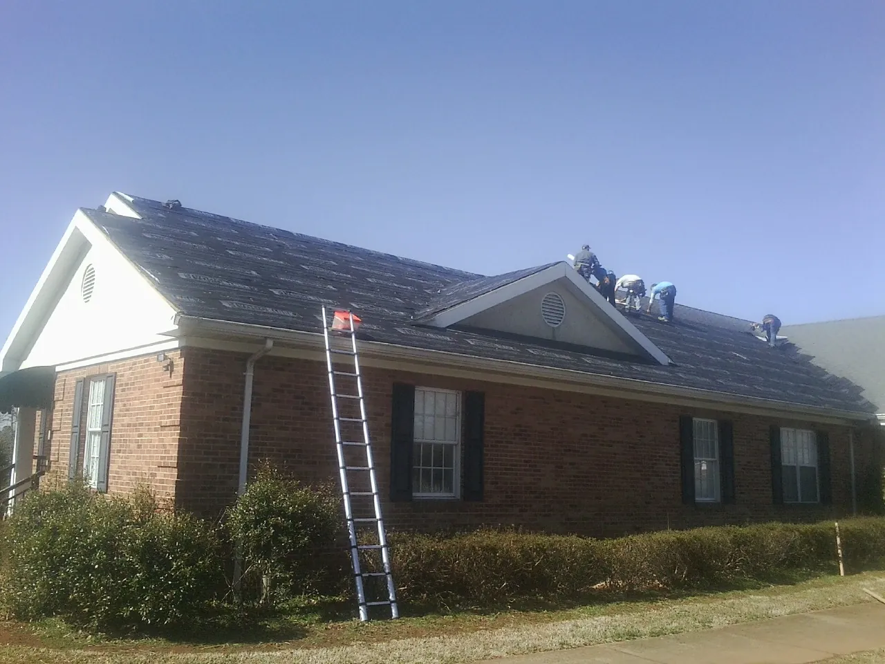 Crew tearing shingles off a brick ranch roof with a ladder set — Emergency Roof Repair work by our crew in Mountain Dale