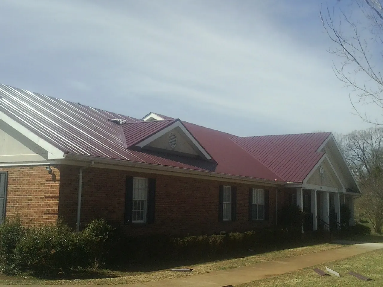 Red metal roof with gabled entries on a long brick building, from a Hail Damage Roof Repair job in Mountain Dale