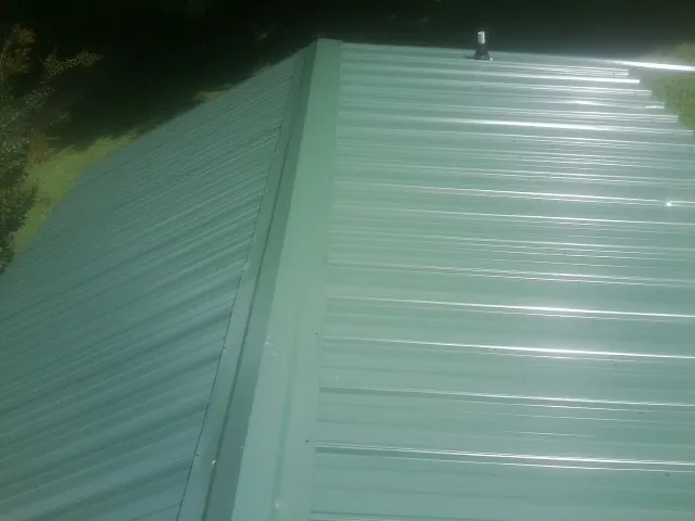 New green metal panels meeting at the ridge of a roof — Flat Roof Repair work by our crew in Mountain Dale