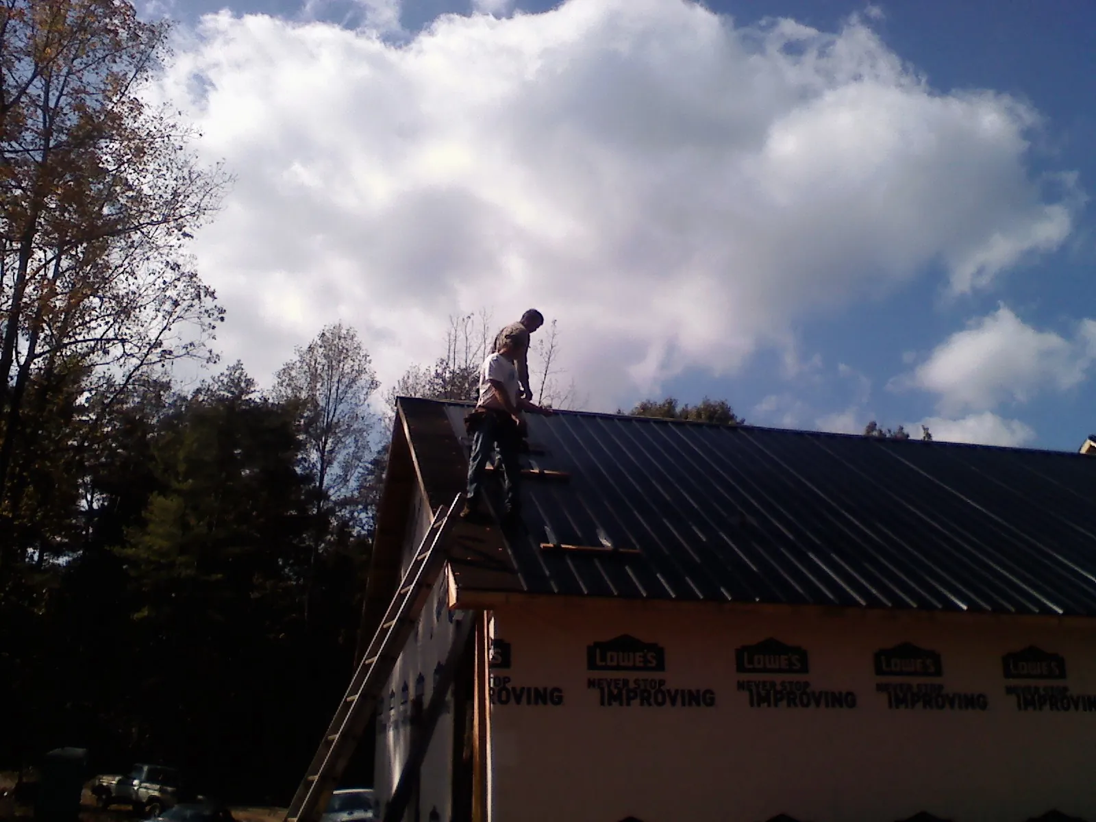 Roofer fastening dark metal panels high against a cloudy sky, from a Roof Inspection job in Mountain Dale