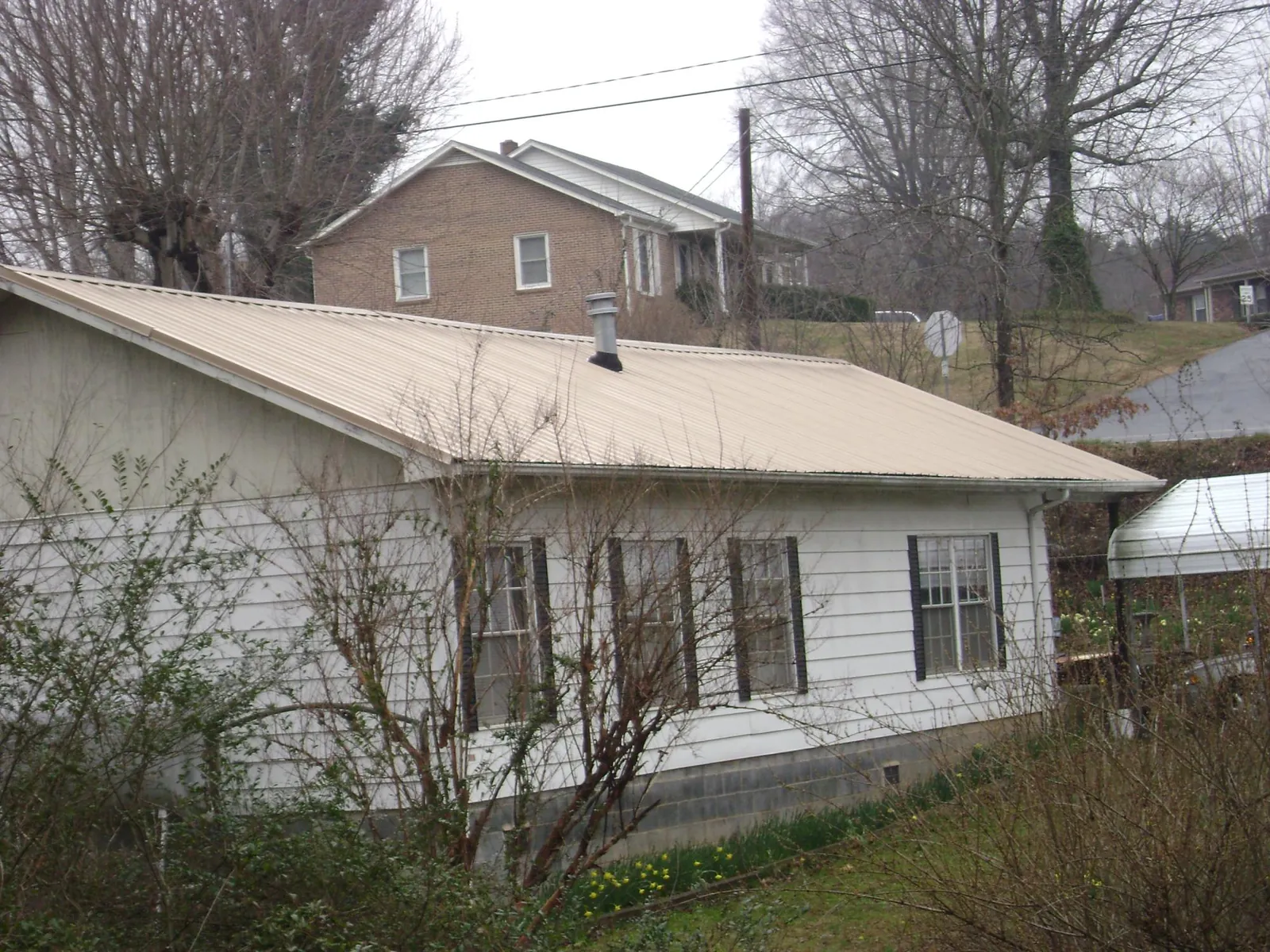 Tan metal roof on a white sided house set into a hillside — Commercial Roofing by Roofing Brothers in Mountain Dale