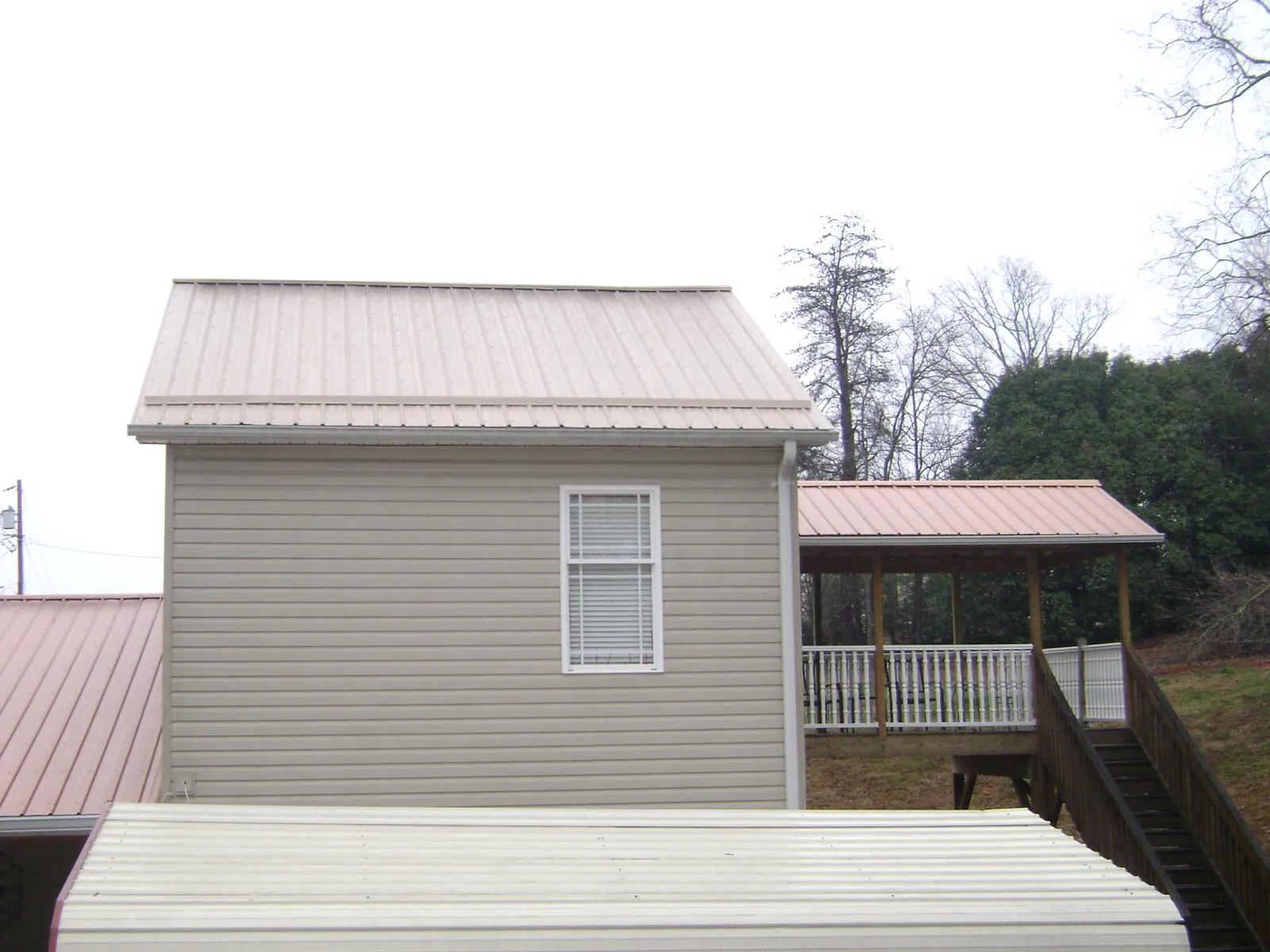 Tan metal roofs on a two story addition and attached porch, from a Roof Replacement job in Mountain Dale